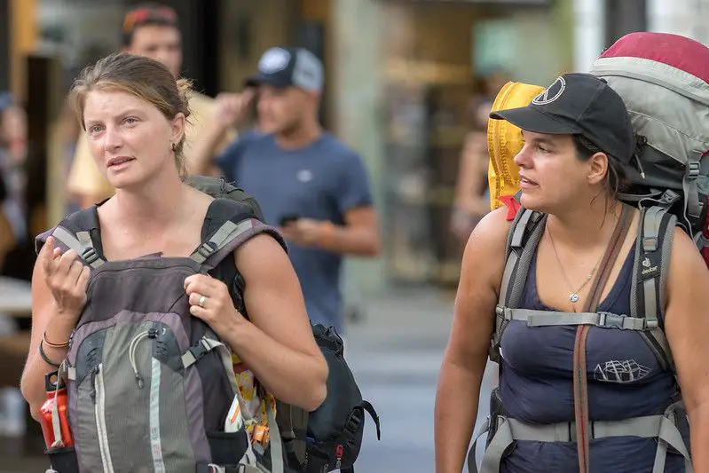 two women who look tired and are carrying multiple backpacks