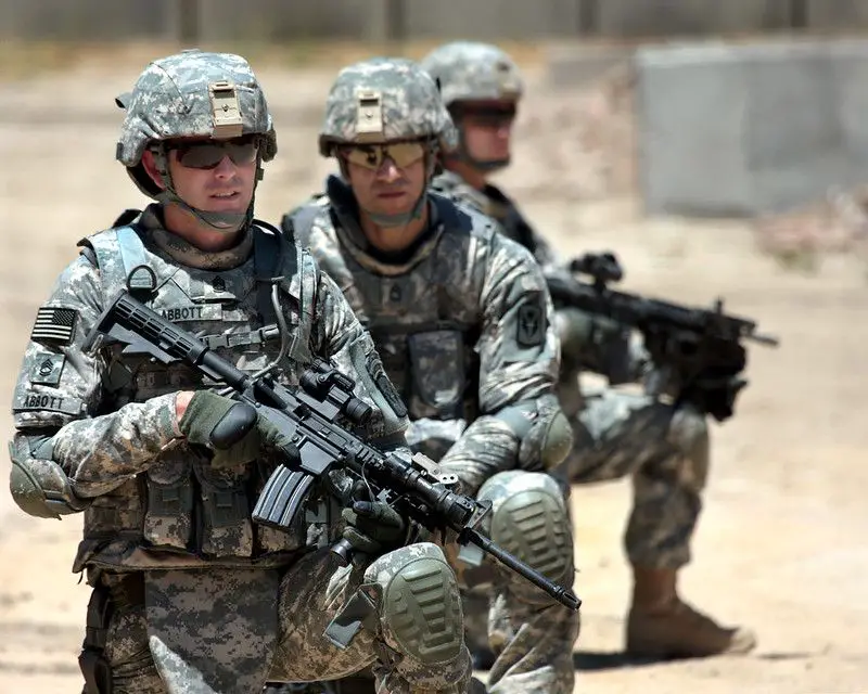 Soldiers kneeling down wearing knee pads while carrying weapons.