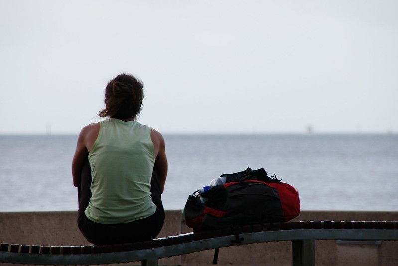 Woman looking out at the water with her rucksack beside her